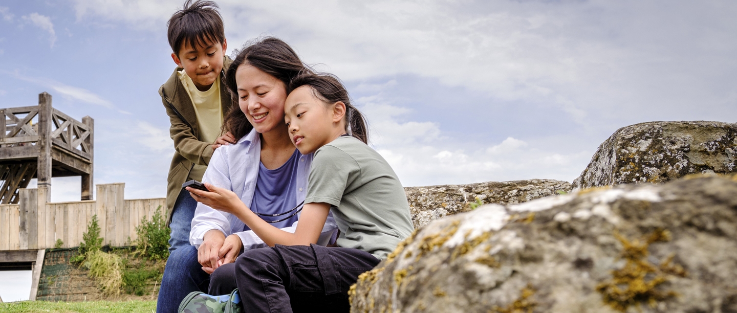 Photo of an adult and two children looking at a smartphone at Richborough Roman Fort